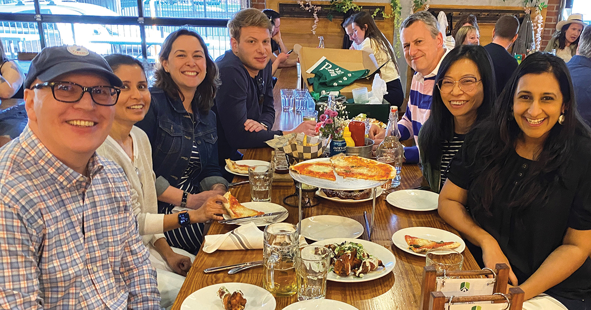 A group of alumni pose for a photo while sitting at a restaurant table